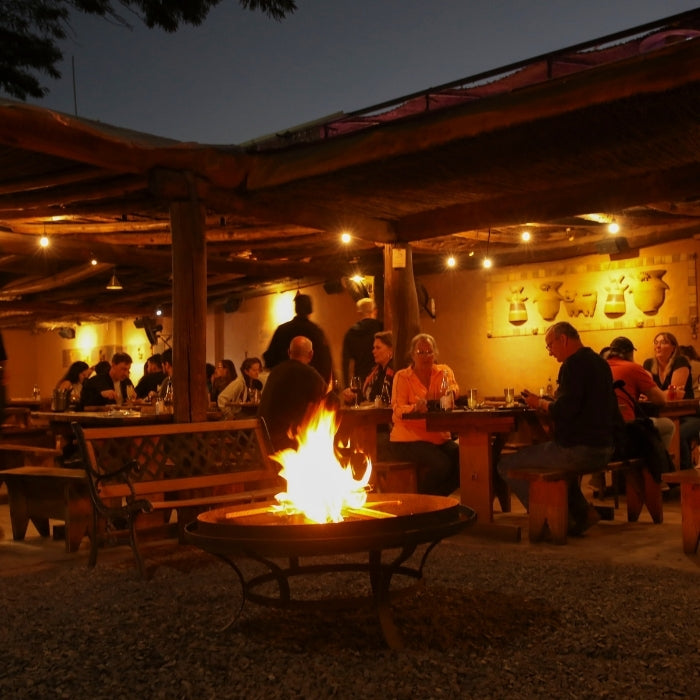 Comedor de Adobe en San Pedro de Atacama, con mesas de madera y fogón central, una experiencia de hospedaje y gastronomía destacada en Bazar ED Edit.