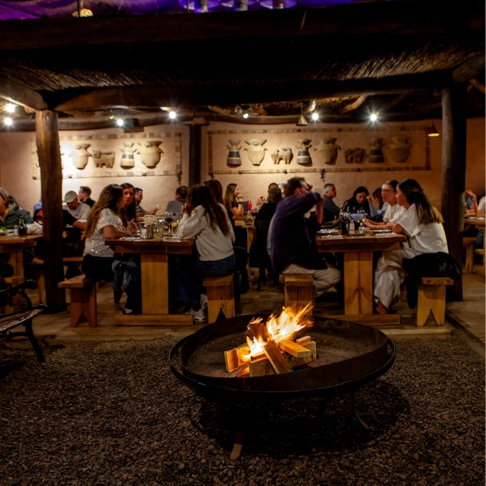 Comedor de Adobe Restaurant en San Pedro de Atacama, con mesas de madera y fogón central, destacado en Bazar ED Edit.